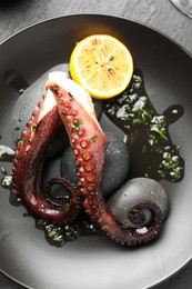 Photo of Fried octopus with herb sauce and lemon served on grey table, top view