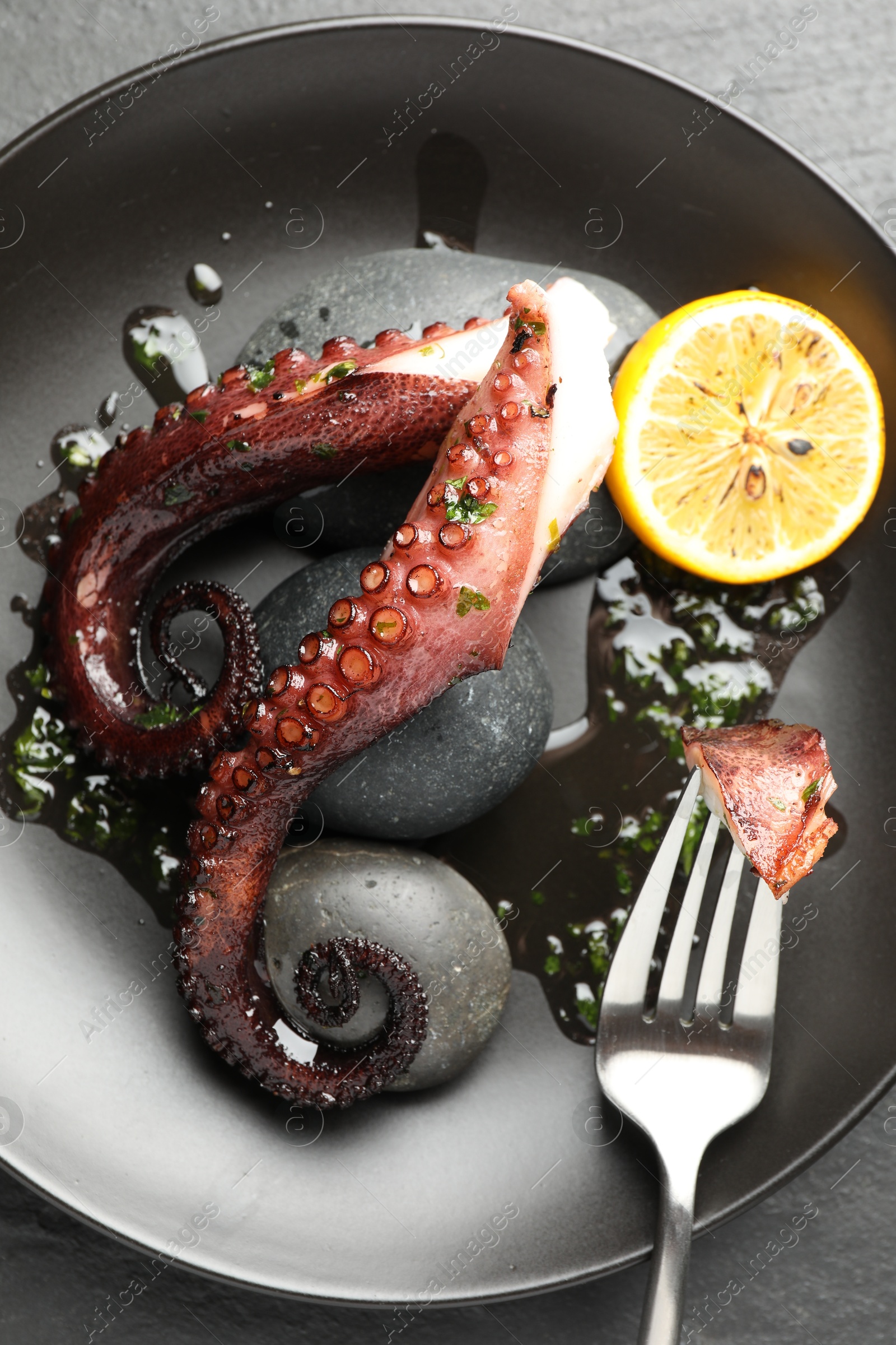 Photo of Fried octopus with herb sauce and lemon served on grey table, top view