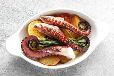 Photo of Fried octopus with vegetables, lemon and rosemary in baking dish on grey textured table, top view