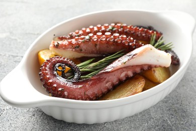 Photo of Fried octopus with potato and rosemary in baking dish on grey textured table, closeup