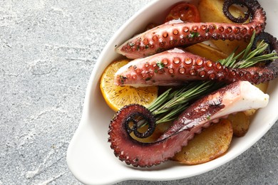 Photo of Fried octopus with vegetables, lemon and rosemary in baking dish on grey textured table, top view. Space for text