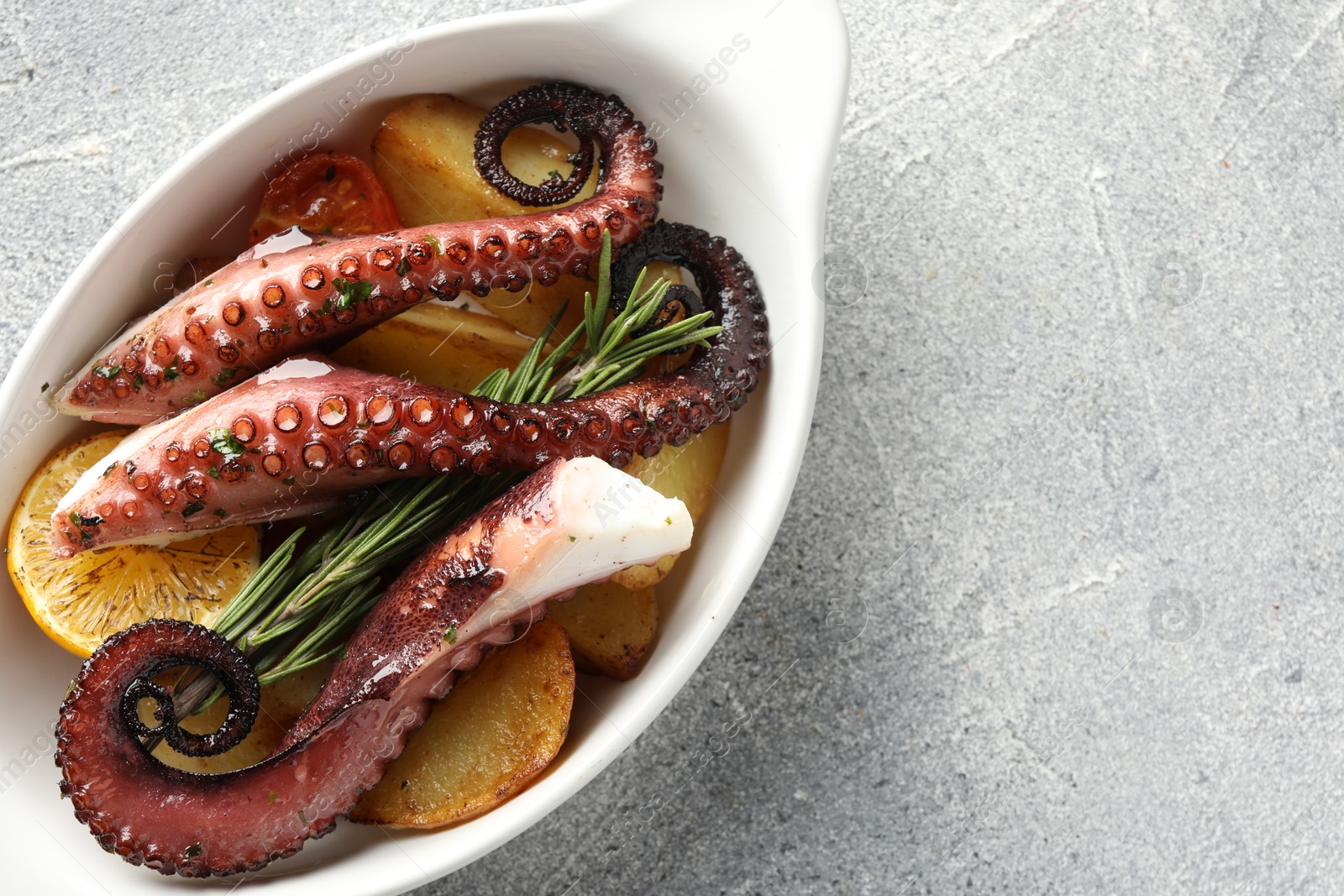 Photo of Fried octopus with vegetables, lemon and rosemary in baking dish on grey textured table, top view. Space for text