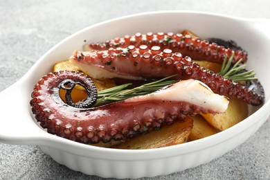 Photo of Fried octopus with potato and rosemary in baking dish on grey textured table, closeup