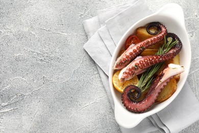 Photo of Fried octopus with vegetables, lemon and rosemary in baking dish on grey textured table, top view. Space for text