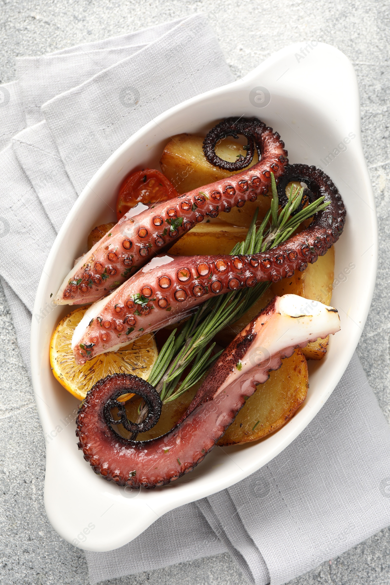 Photo of Fried octopus with vegetables, lemon and rosemary in baking dish on grey textured table, top view