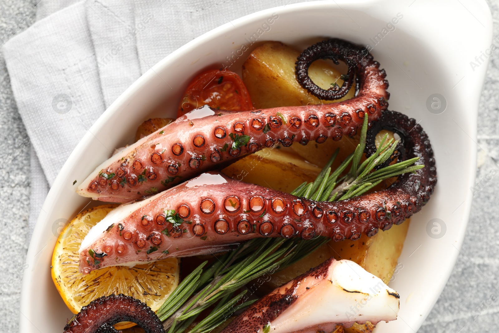 Photo of Fried octopus with vegetables, lemon and rosemary in baking dish on grey textured table, top view