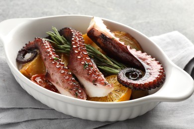 Photo of Fried octopus with vegetables, lemon and rosemary in baking dish on table, closeup