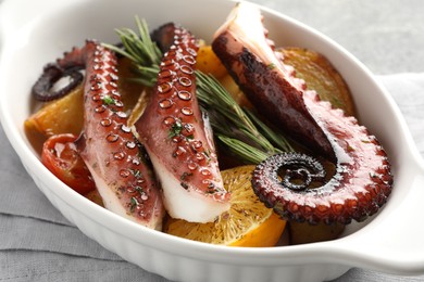 Photo of Fried octopus with vegetables, lemon and rosemary in baking dish on table, closeup