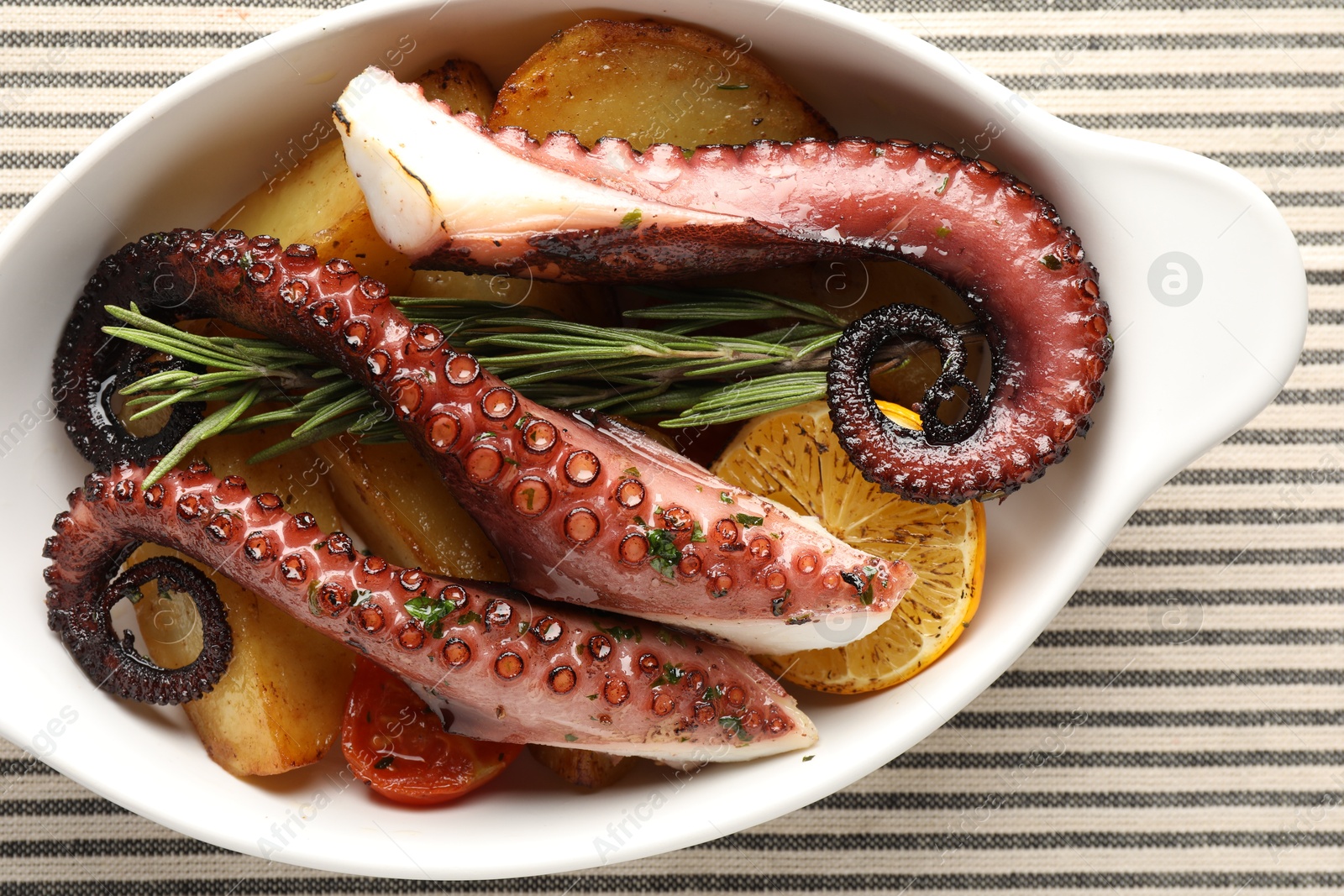 Photo of Fried octopus with vegetables, lemon and rosemary in baking dish on tablecloth, top view