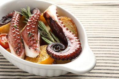 Photo of Fried octopus with vegetables, lemon and rosemary in baking dish on tablecloth, closeup