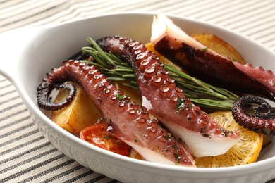 Photo of Fried octopus with vegetables, lemon and rosemary in baking dish on tablecloth, closeup