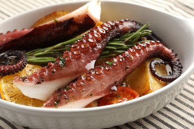 Photo of Fried octopus with vegetables, lemon and rosemary in baking dish on tablecloth, closeup