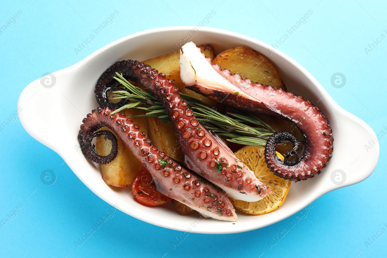 Photo of Fried octopus with vegetables, lemon and rosemary in baking dish on light blue background, top view