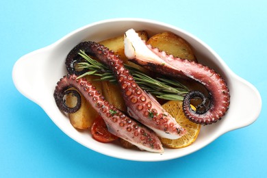 Photo of Fried octopus with vegetables, lemon and rosemary in baking dish on light blue background, top view