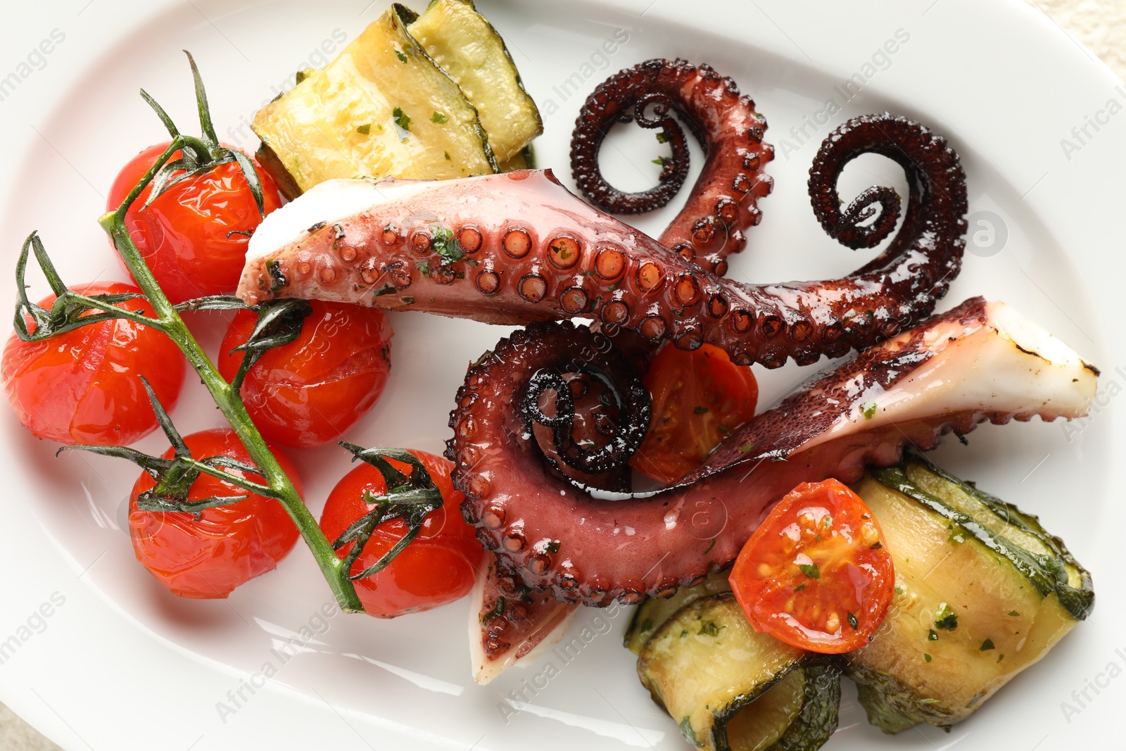 Photo of Fried octopus with zucchini and tomatoes on plate, top view