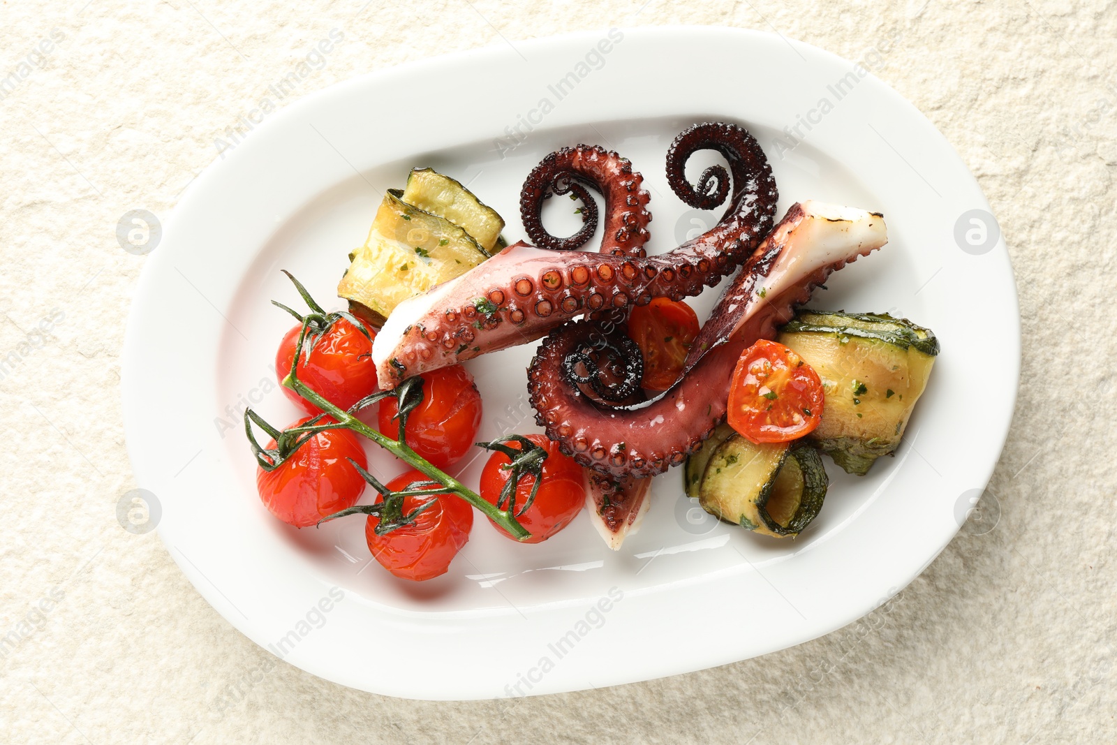 Photo of Fried octopus with zucchini and tomatoes on light textured table, top view