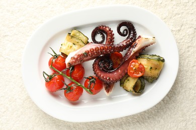 Photo of Fried octopus with zucchini and tomatoes on light textured table, top view