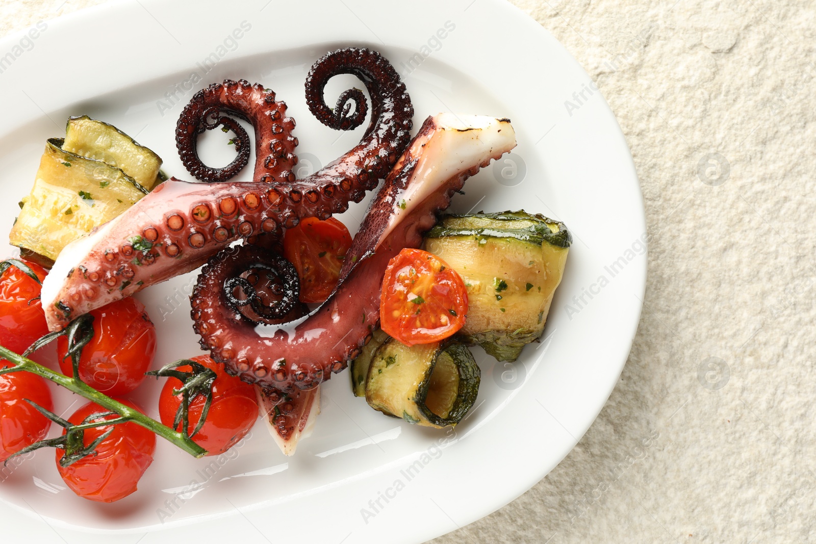 Photo of Fried octopus with zucchini and tomatoes on light textured table, top view