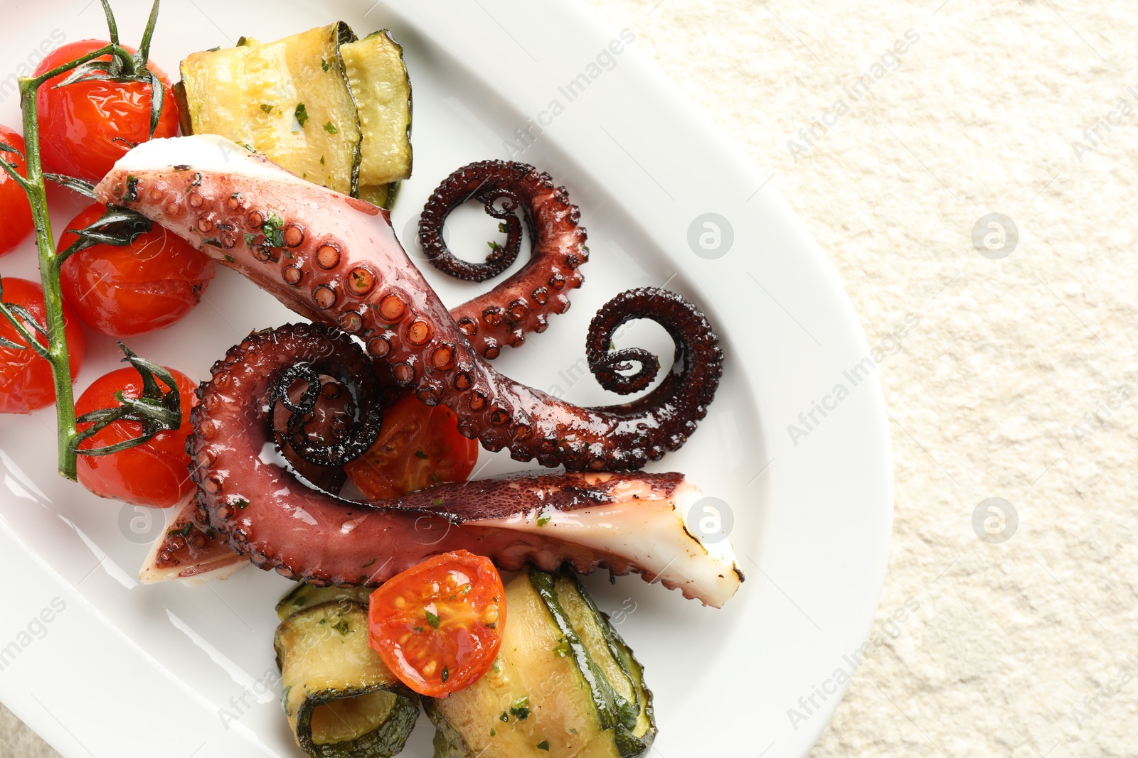 Photo of Fried octopus with zucchini and tomatoes on light textured table, top view