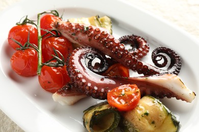 Photo of Fried octopus with zucchini and tomatoes on light table, closeup