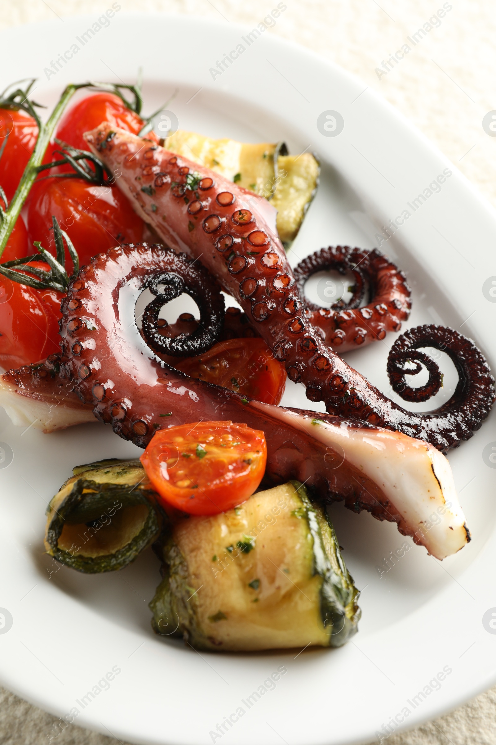 Photo of Fried octopus with zucchini and tomatoes on light table, closeup