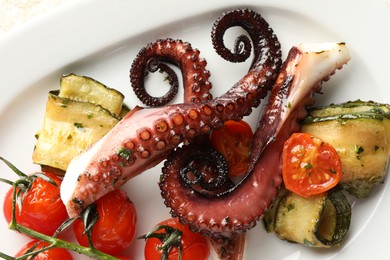 Photo of Fried octopus with zucchini and tomatoes on plate, top view