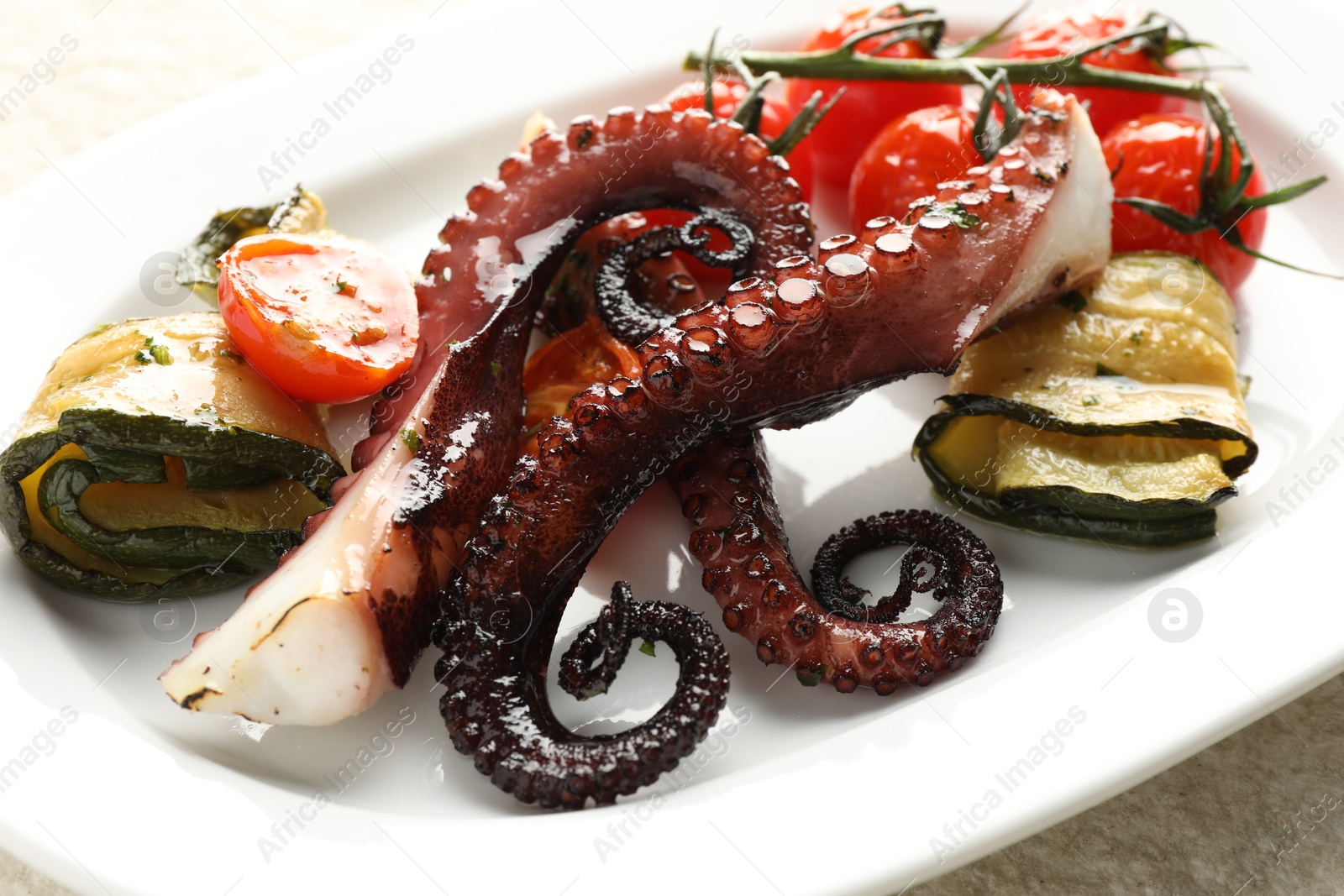 Photo of Fried octopus with zucchini and tomatoes on light textured table, closeup