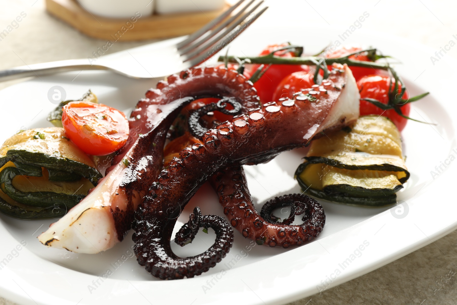 Photo of Fried octopus with zucchini and tomatoes on light textured table, closeup