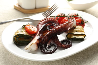 Photo of Fried octopus with zucchini and tomatoes on light textured table, closeup