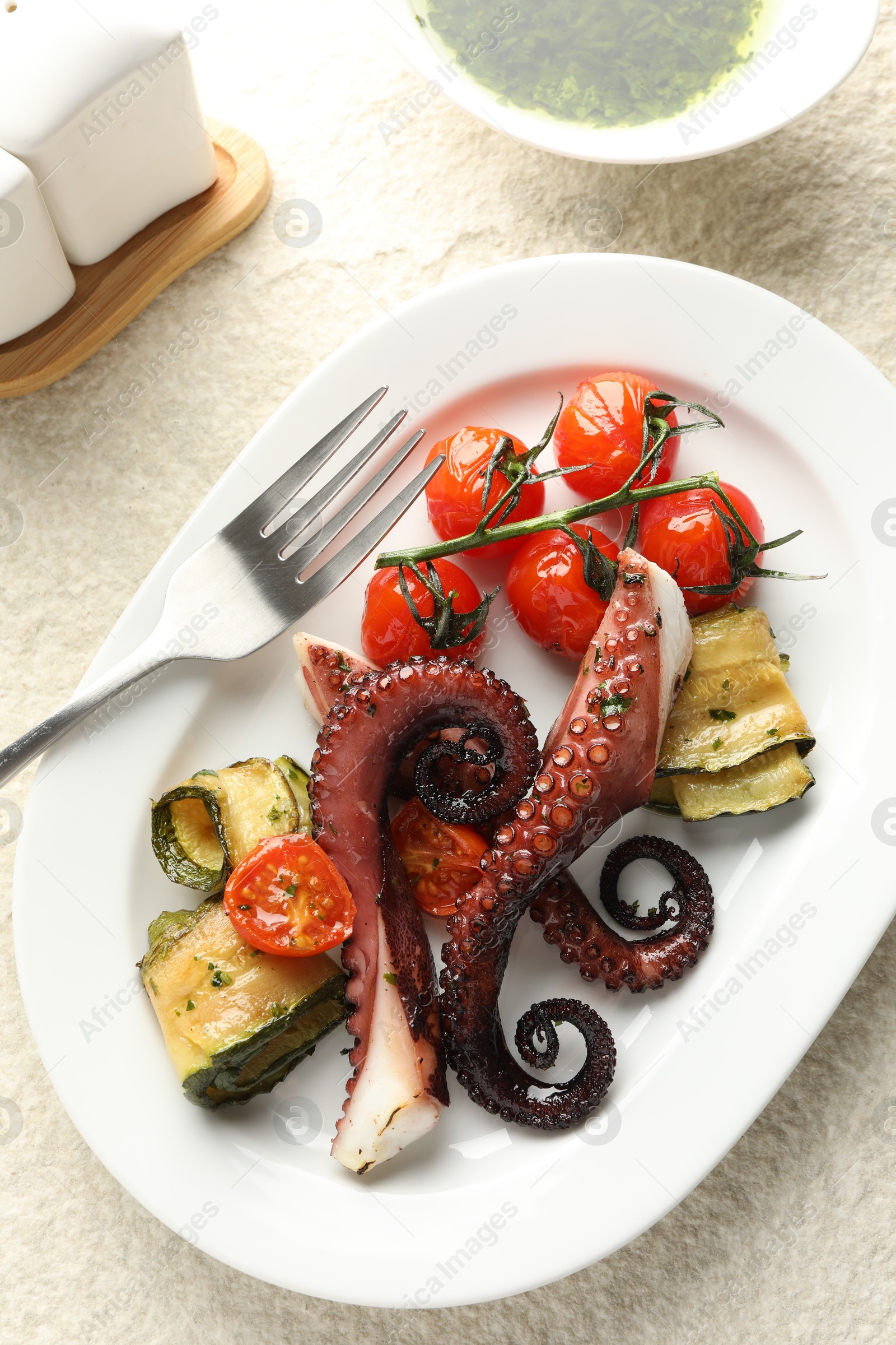 Photo of Fried octopus with herb sauce, zucchini and tomatoes on light textured table, flat lay