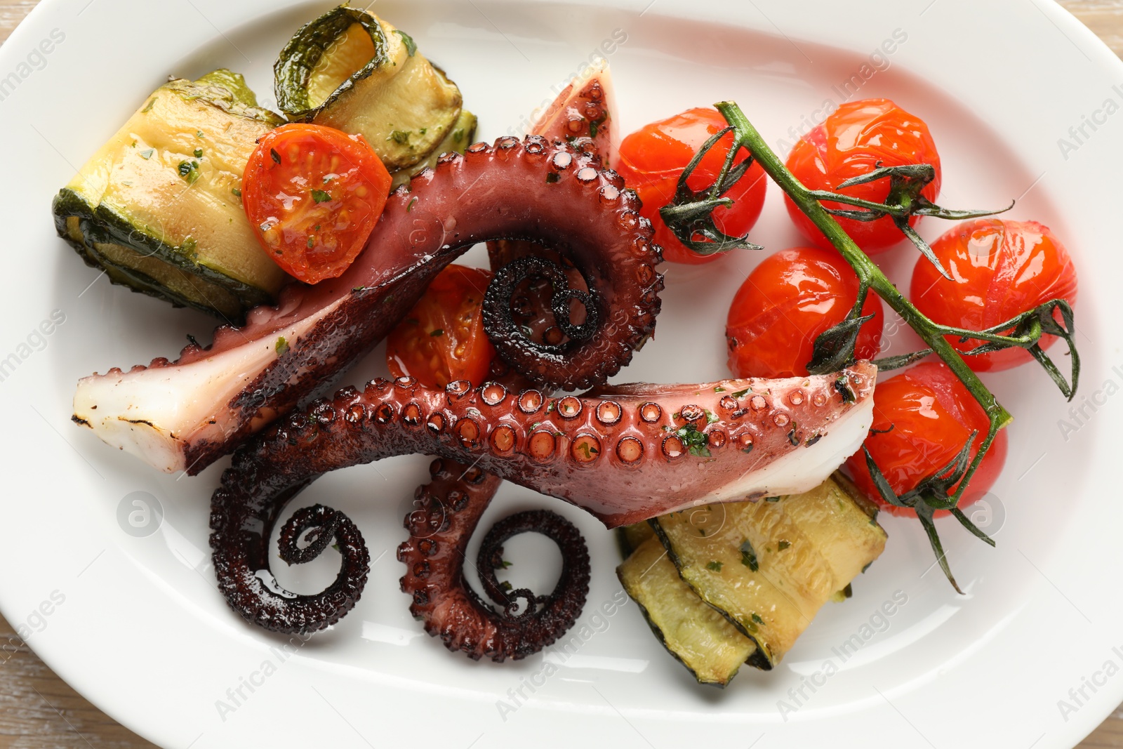 Photo of Fried octopus with zucchini and tomatoes on wooden table, top view