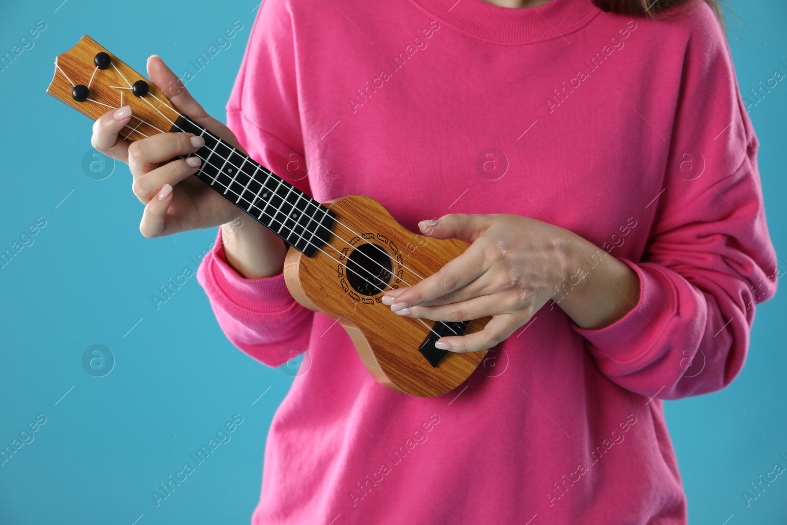 Photo of Woman playing ukulele on light blue background, closeup