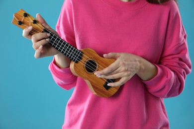 Photo of Woman playing ukulele on light blue background, closeup