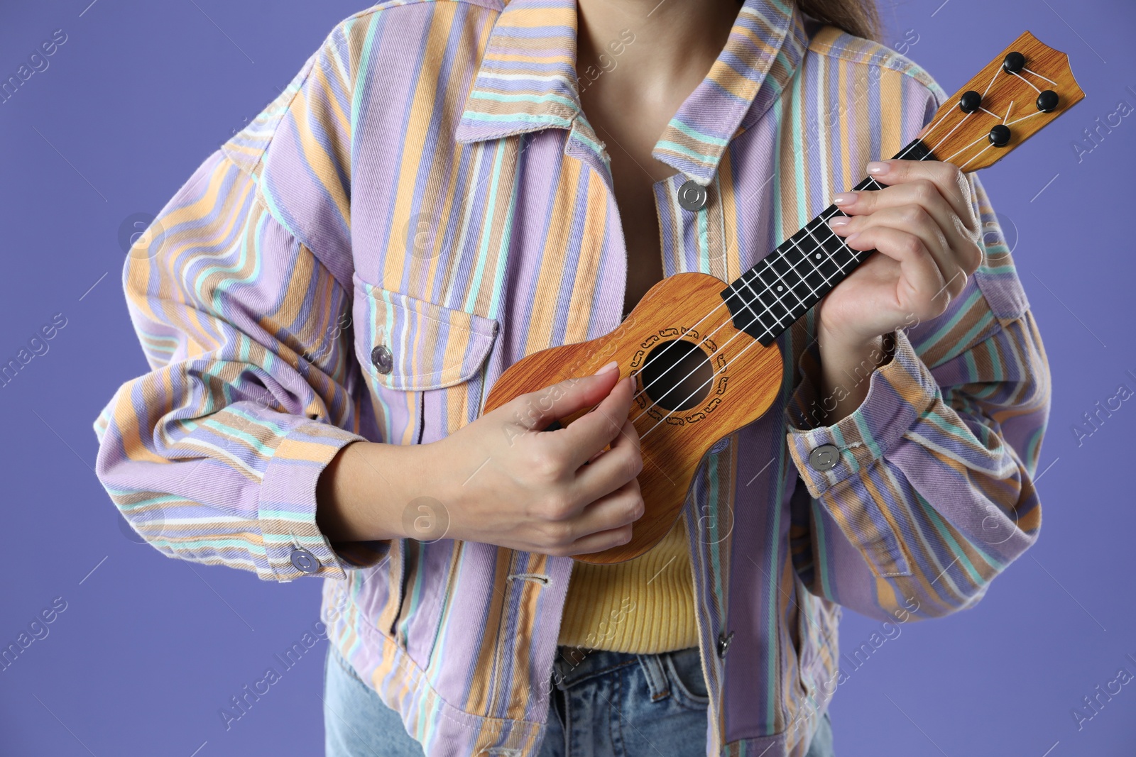 Photo of Woman playing ukulele on purple background, closeup