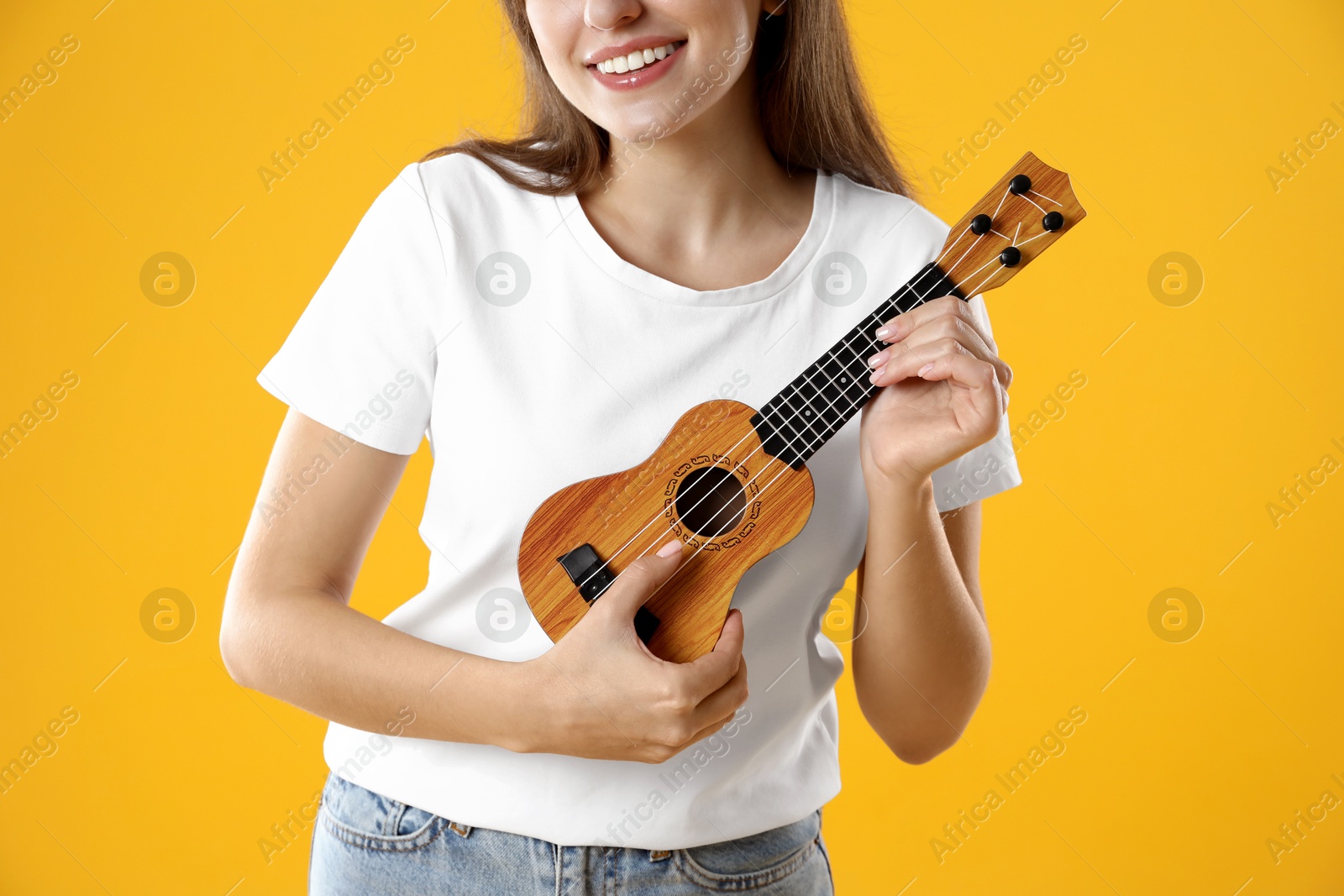 Photo of Woman playing ukulele on orange background, closeup