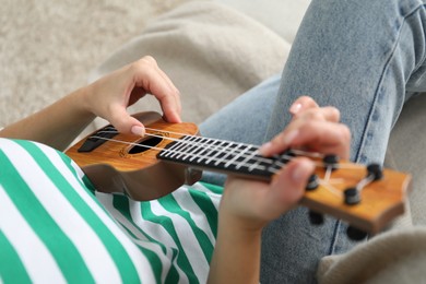 Photo of Woman playing ukulele on sofa at home, closeup