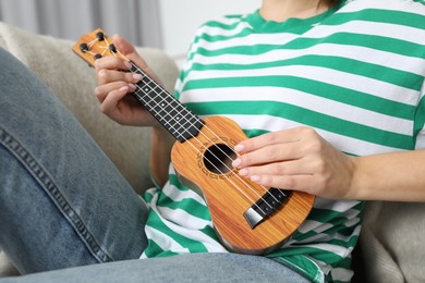 Photo of Woman playing ukulele on sofa at home, closeup