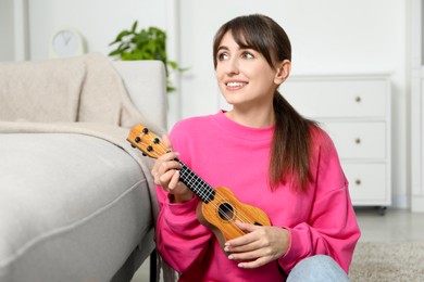 Photo of Happy woman playing ukulele on floor at home