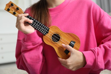 Photo of Woman playing ukulele at home, closeup view