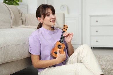 Photo of Happy woman playing ukulele on floor at home