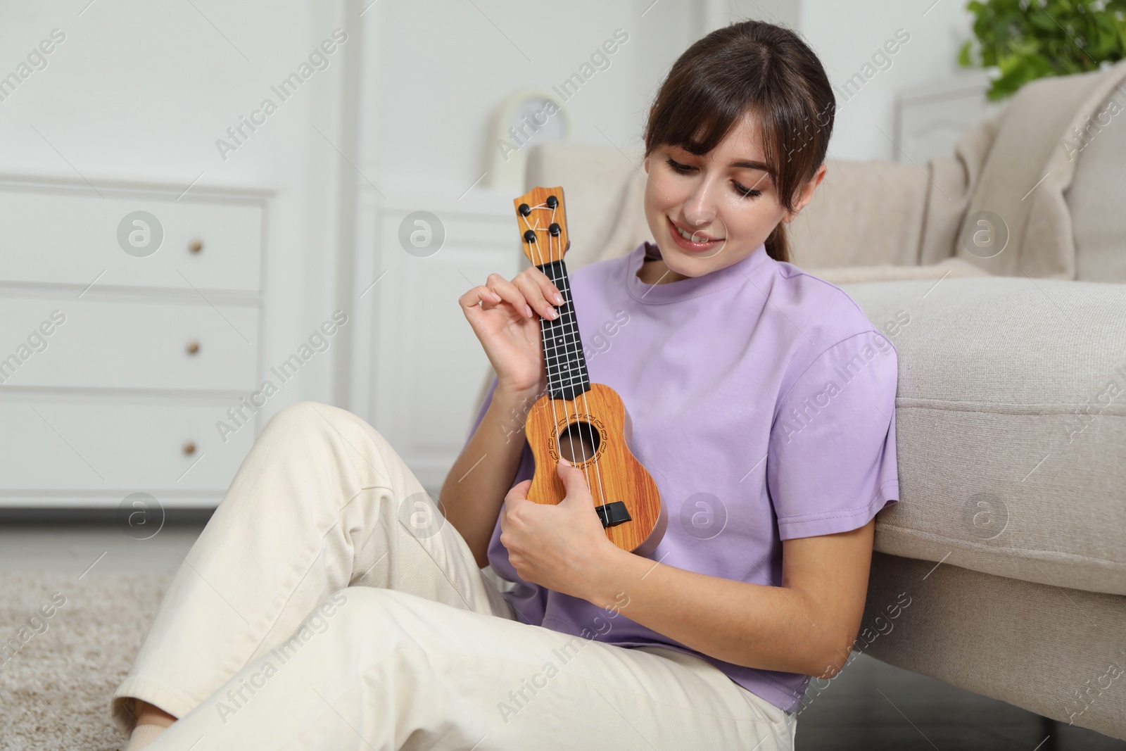 Photo of Happy woman playing ukulele on floor at home