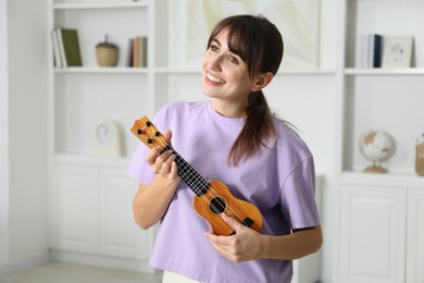 Photo of Happy young woman playing ukulele at home