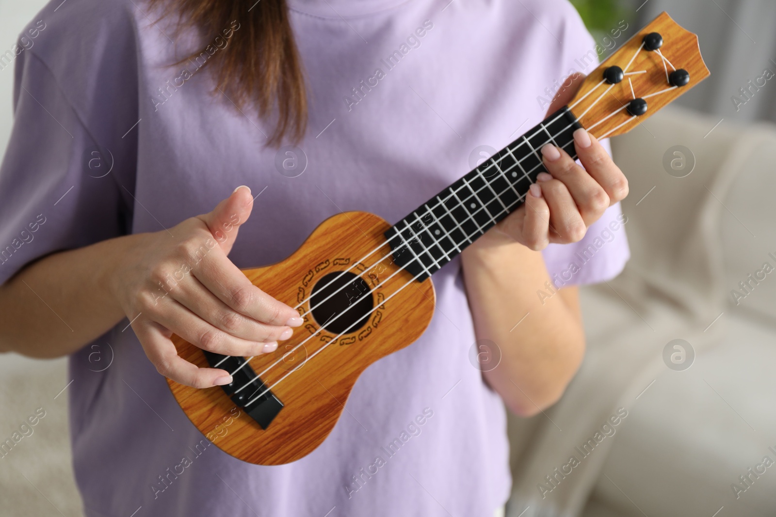 Photo of Woman playing ukulele at home, closeup view