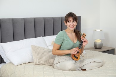 Photo of Happy woman playing ukulele on bed at home