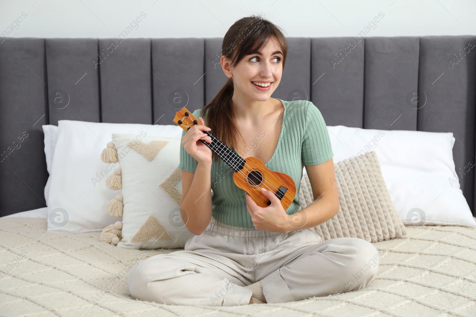 Photo of Happy woman playing ukulele on bed at home