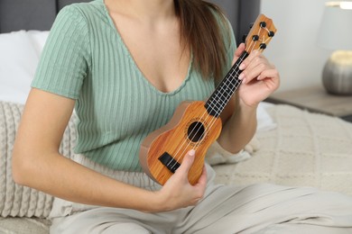 Photo of Woman playing ukulele on bed at home, closeup