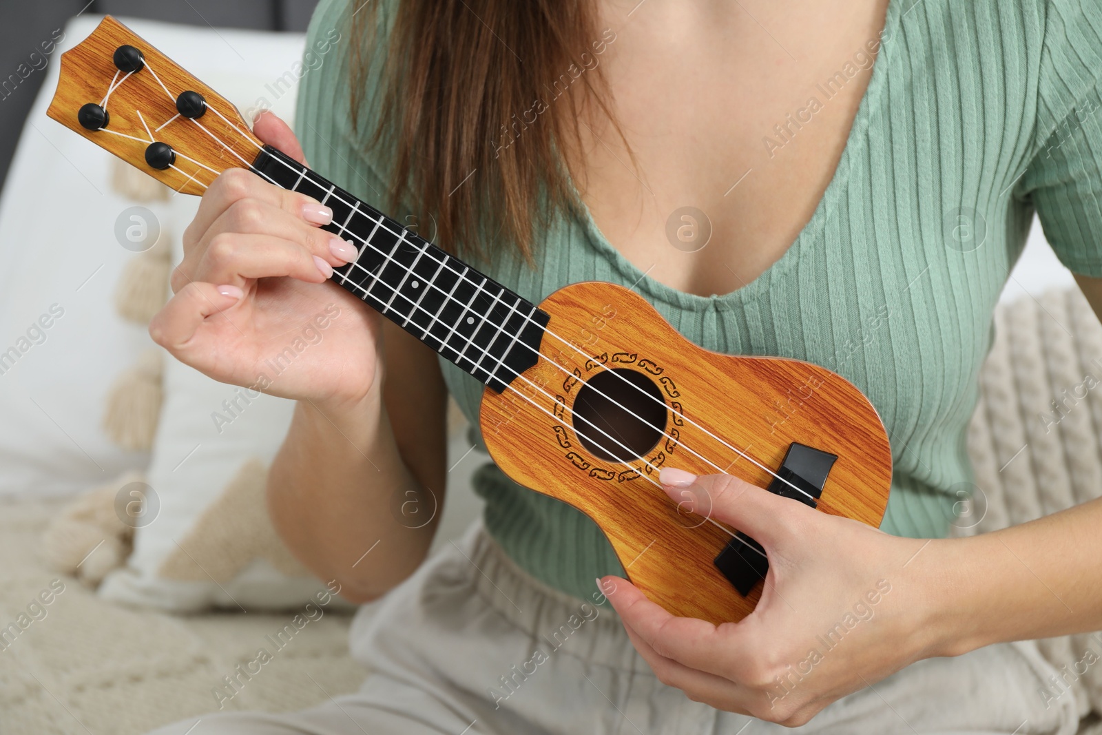 Photo of Woman playing ukulele on bed at home, closeup