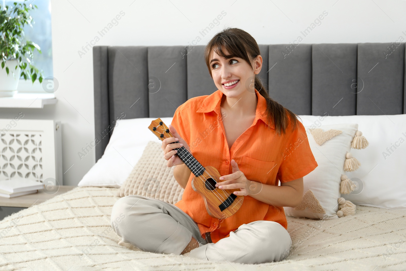 Photo of Happy woman playing ukulele on bed at home