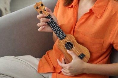 Photo of Woman playing ukulele in armchair at home, closeup