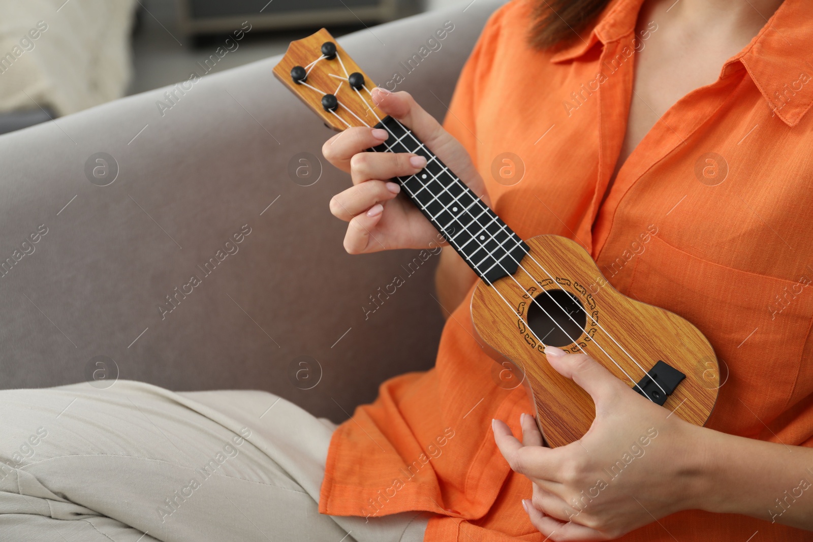 Photo of Woman playing ukulele in armchair at home, closeup